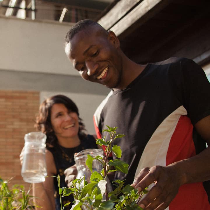 Two people smiling together outdoors, tending to plants.