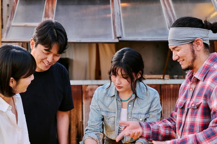 Goseong host smiling and talking with guests outdoors beside a rustic wooden building
