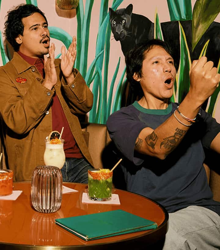 Excited fans cheering in a cozy lounge, shouting and clapping over cocktails.