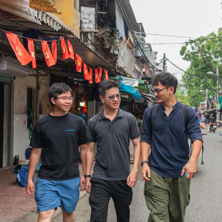 Quang leading an Airbnb Experience walk in Hanoi, passing family-run businesses and flags on a narrow street