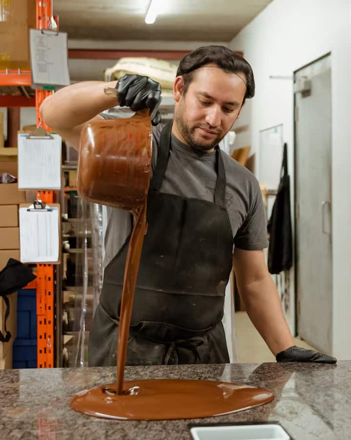 Chocolate maker in a Toronto kitchen pouring melted chocolate onto a marble counter