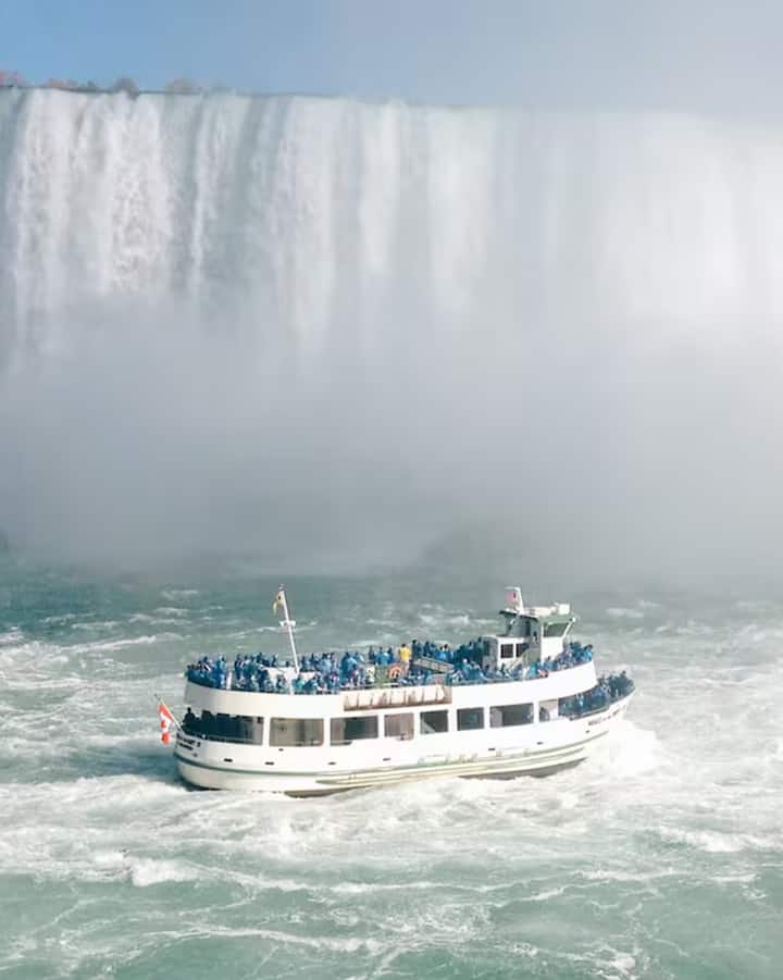 Tour boat packed with visitors in blue ponchos approaching the misty base of Niagara Falls in Toronto area