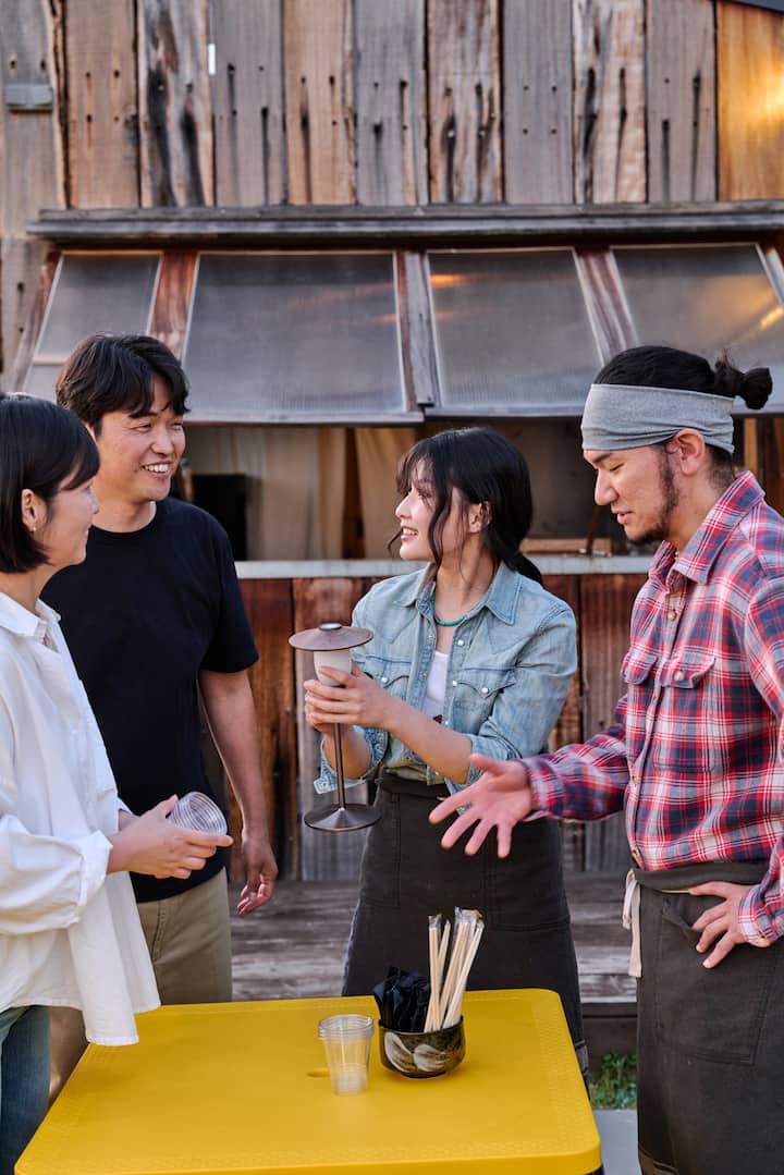 Goseong hosts smiling with visitors in front of a rustic wooden building.