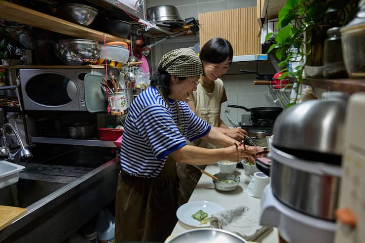 Suncheon host teaches a guest to cook in a cozy, cluttered kitchen