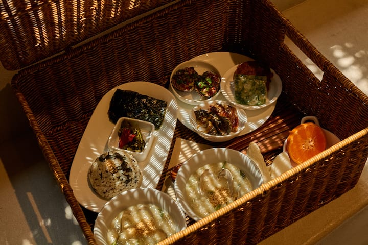 Traditional Korean breakfast basket prepared by a Suncheon host, with rice, soup, side dishes, and fruit in warm sunlight.