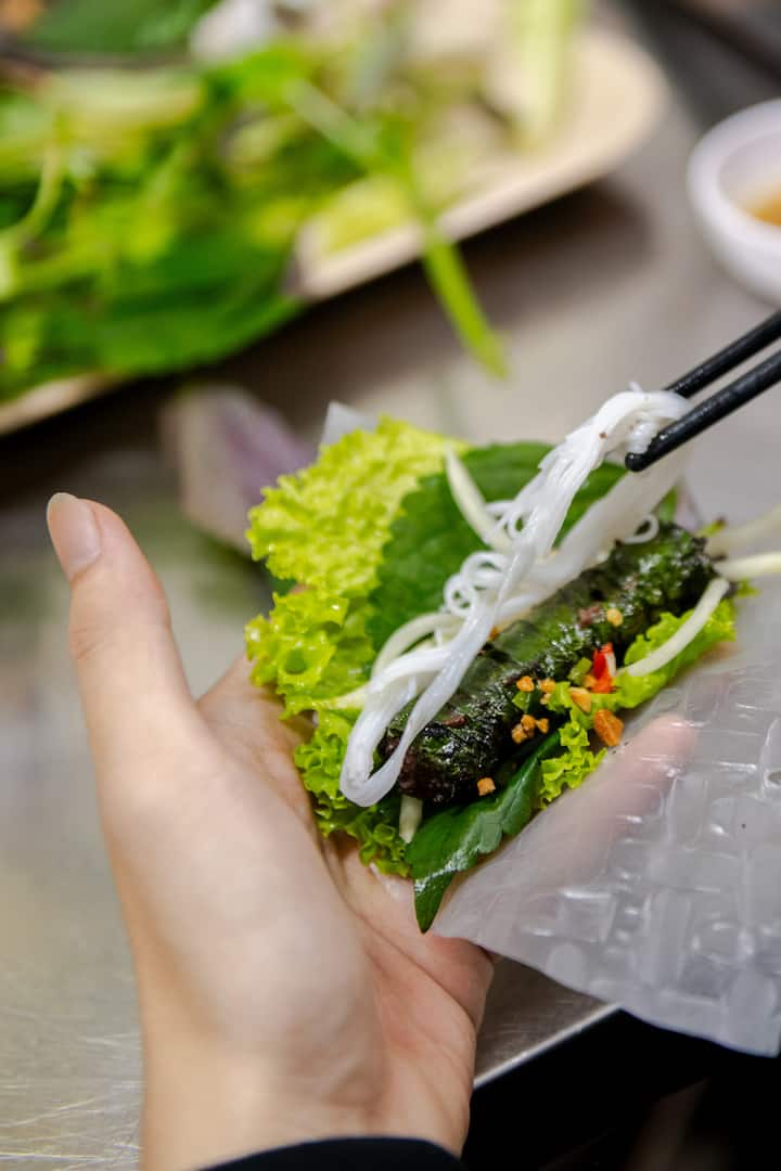 Hand assembling Vietnamese rice paper roll with herbs, grilled meat, and noodles for Khoi’s host experience