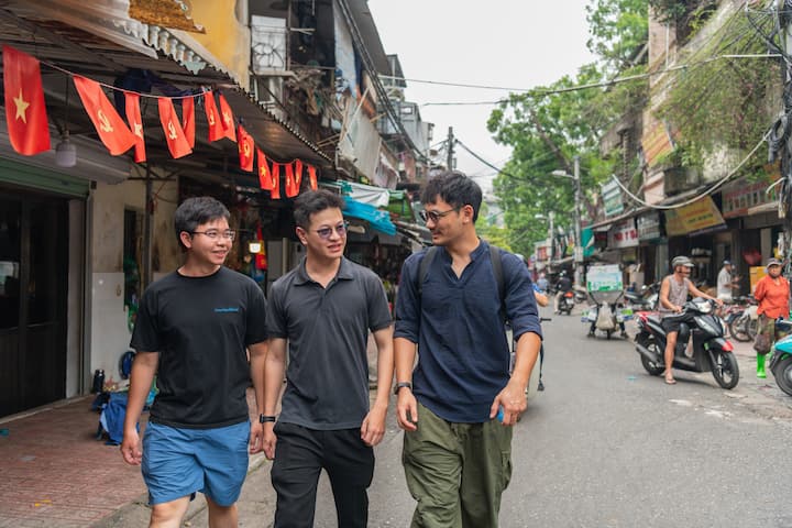 Quang and two friends walking down a busy street in Vietnam lined with shops and flags