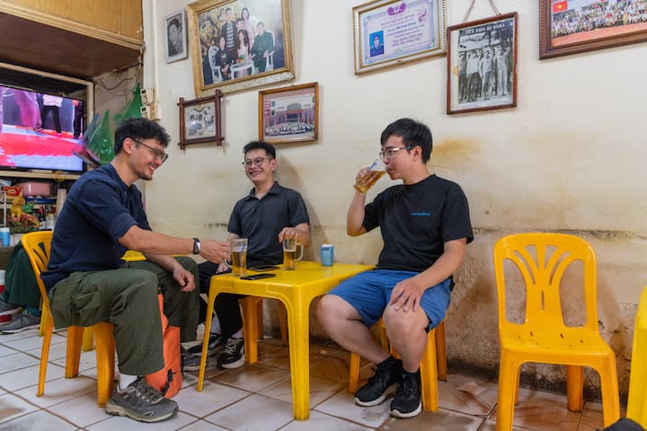 Quang sits with two friends on yellow plastic chairs, laughing and drinking beer in a modest Vietnam café.