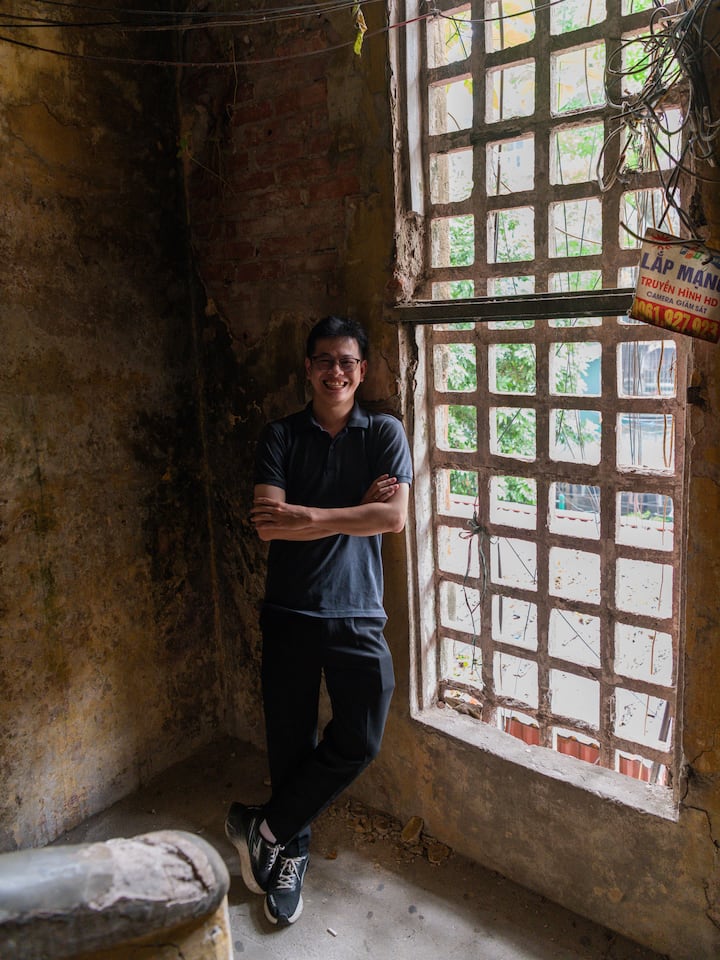 Quang stands smiling by a rustic grid window