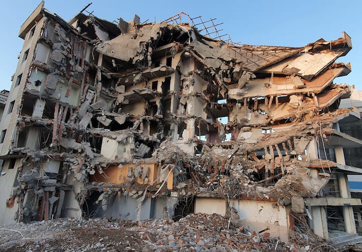 Collapsed apartment building with exposed rooms and rubble, illustrating earthquake damage in Southeast Asia for Airbnb.org relief.