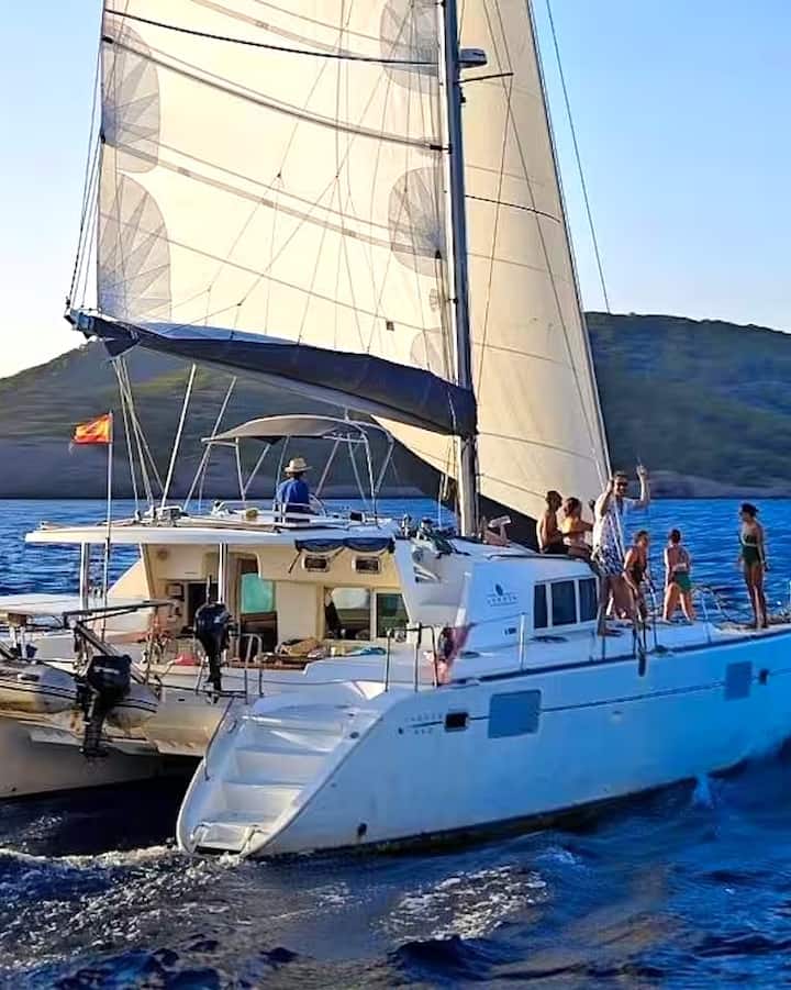 Unos viajeros relajándose y pasándoselo bien en un velero blanco frente a la costa rocosa entre Mallorca e Ibiza.