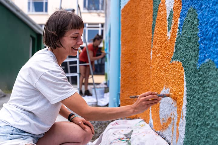 Smiling woman painting a colorful rural mural, representing Airbnb’s Rural Tourism Fund community support