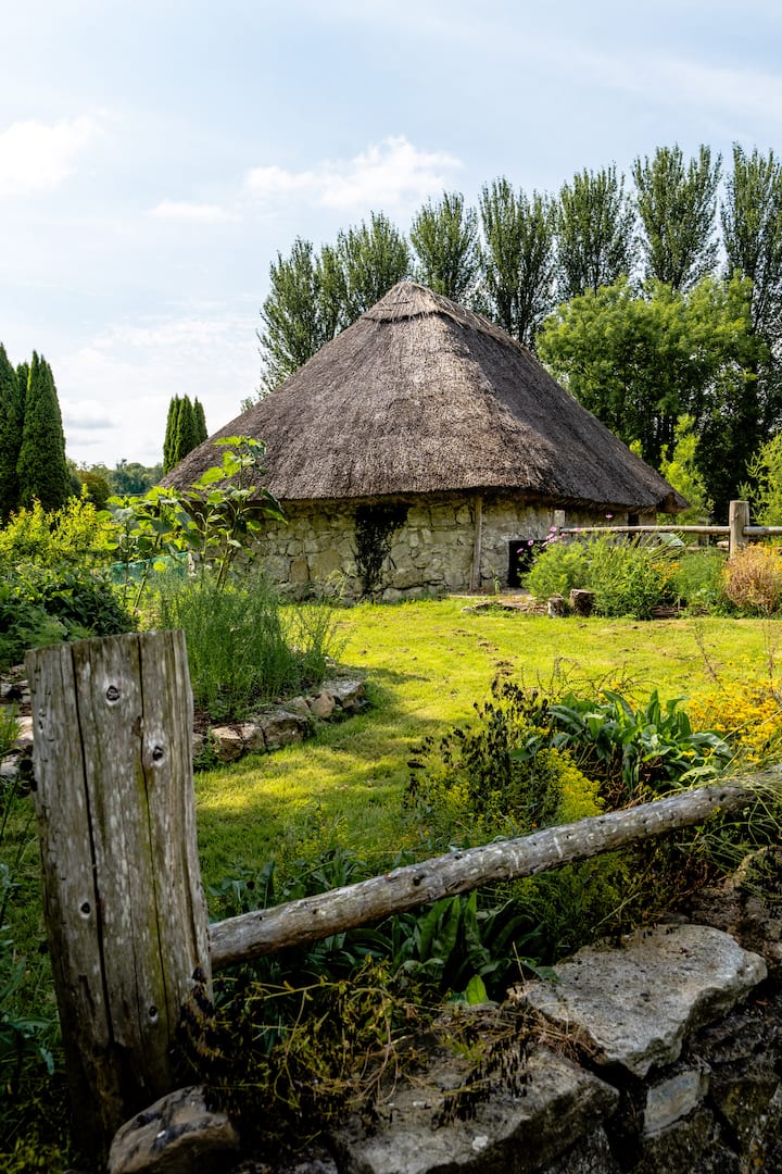 Stone cottage with a thatched roof surrounded by lush garden, illustrating rural stays supported by the Tourism Fund