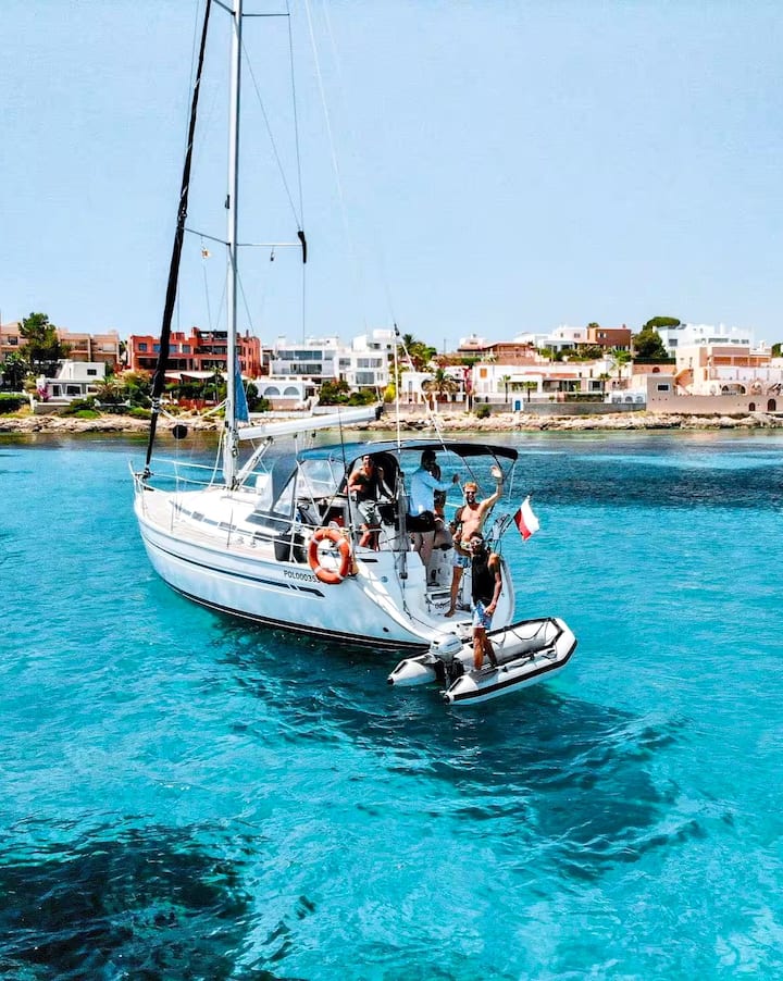 Un velero anclado frente a Ibiza, con personas relajándose en cubierta sobre las claras aguas turquesas del Mediterráneo.