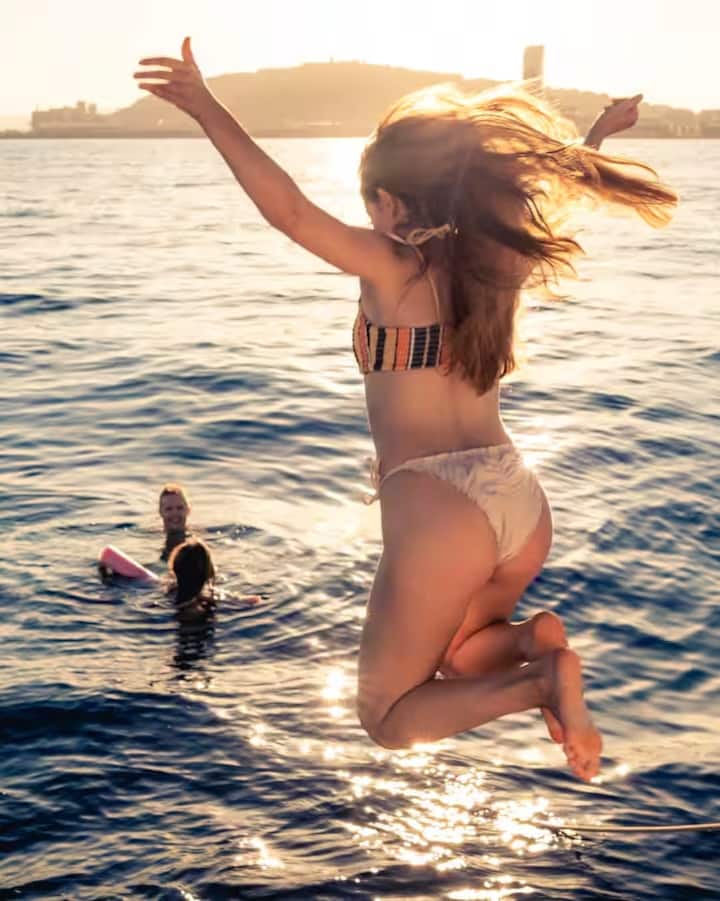 Unos amigos están nadando al atardecer en la costa de Mallorca. Una persona está saltando al mar.