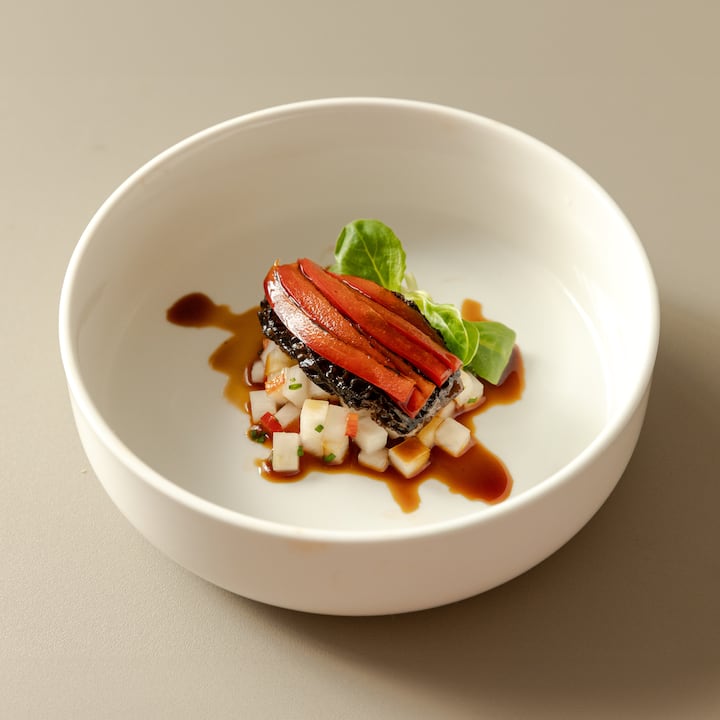 Plated chef-prepared dish with layered vegetables and sauce in a minimalist white bowl
