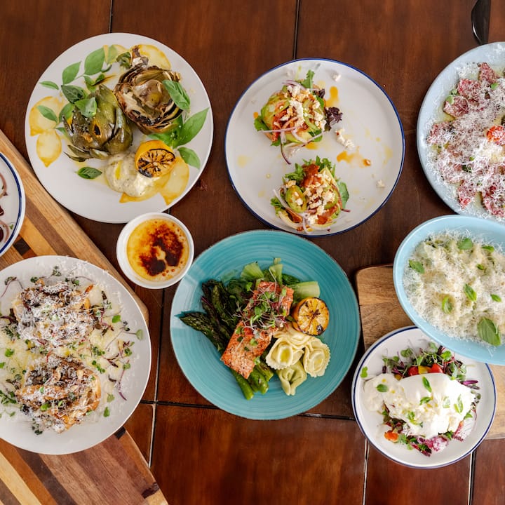 Colorful chef-prepared dinner spread with salmon, grilled vegetables, pasta, salads, and dessert on a wooden table.