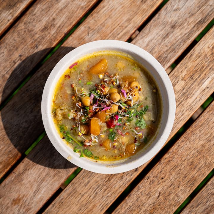 Colorful chickpea and vegetable soup served in a bowl on a rustic wooden table for a catering service.
