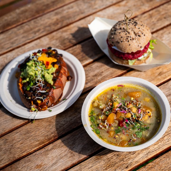 Colorful catered meal with a veggie burger, stuffed sweet potato, and hearty soup on a wooden table.