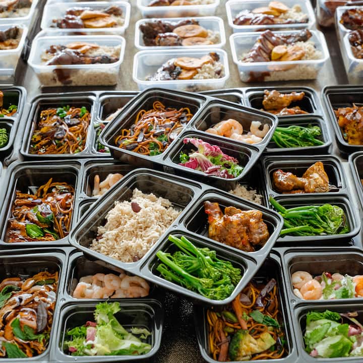 Assorted catered meal boxes filled with rice, noodles, vegetables, shrimp, and chicken arranged in rows.