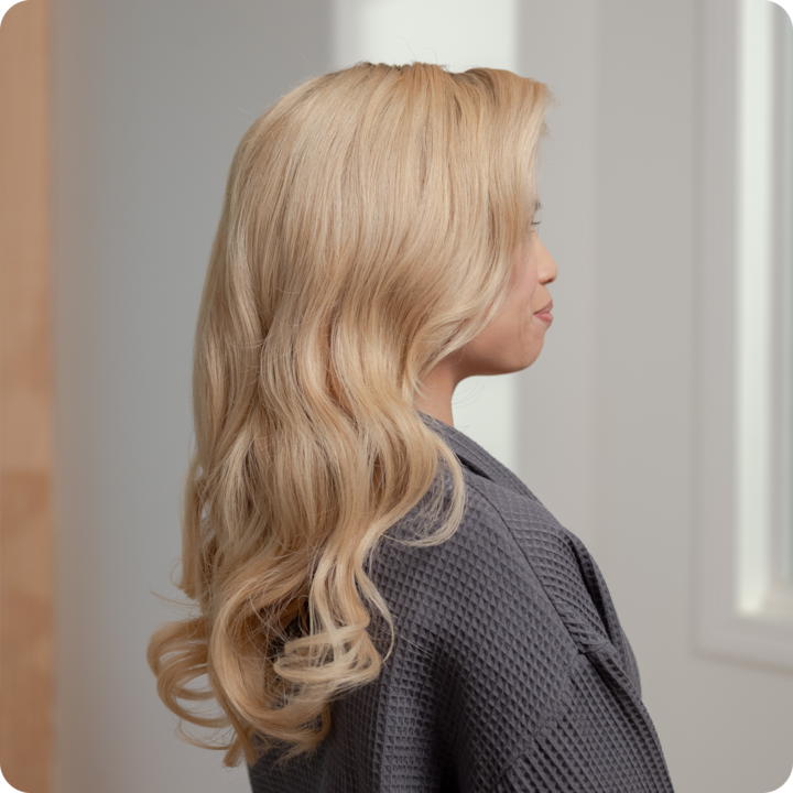 Person with long, wavy blonde hair in a robe, showcasing a fresh professional hairstyle service.