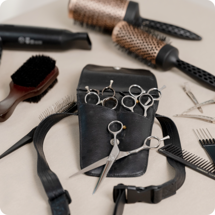 Professional hairstyling tools laid out, with scissors in a leather belt surrounded by brushes, combs, and clips.