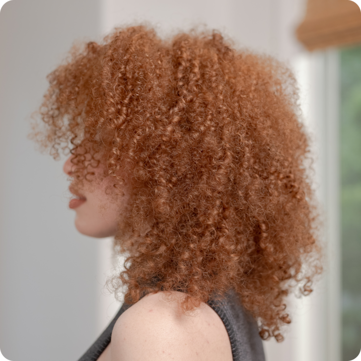 Person with voluminous curly auburn hair, styled naturally, highlighting a beauty service offering