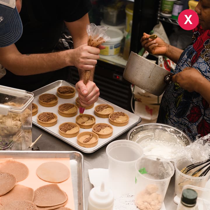 Close-up of hosts piping chocolate filling into mini tart shells during a kitchen photoshoot showcasing their culinary skills.