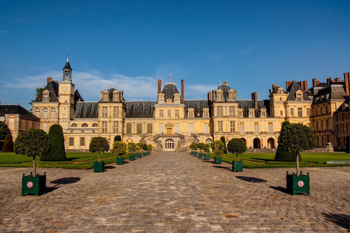 Fontainebleau castle courtyard with manicured gardens under a clear blue sky, highlighting royal architecture near Paris