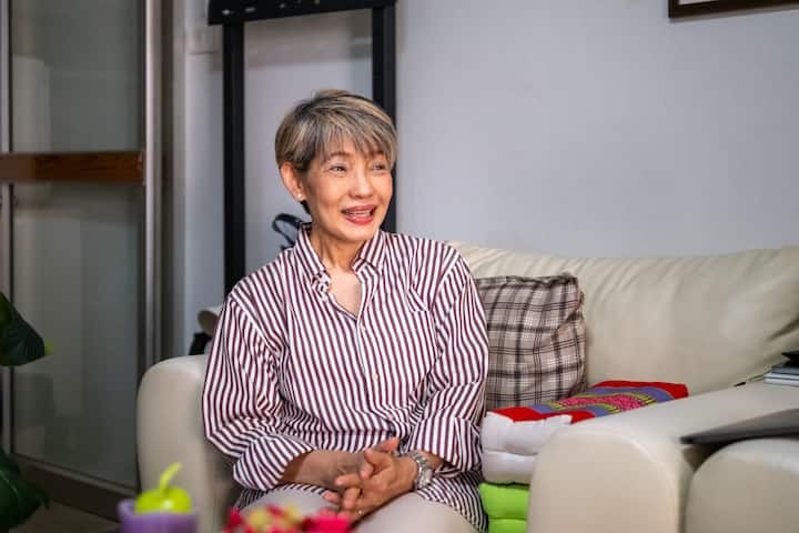 Smiling Thailand host in a striped shirt sits on a sofa, sharing her niche hosting story.