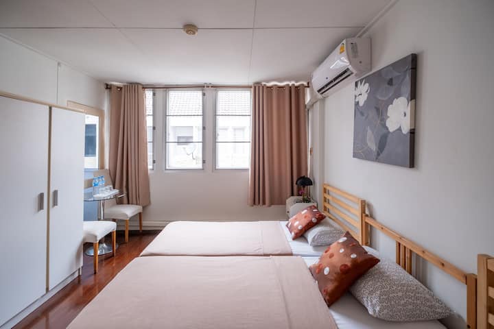 Quiet twin-bed room at Maya Suite with soft pink bedding, neutral curtains, and simple decor for restful hospital stays nearby.