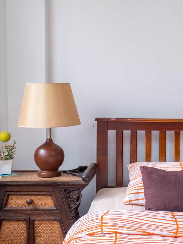 Cozy Thai bedroom with wooden bed, striped orange bedding, and bedside lamp on carved nightstand
