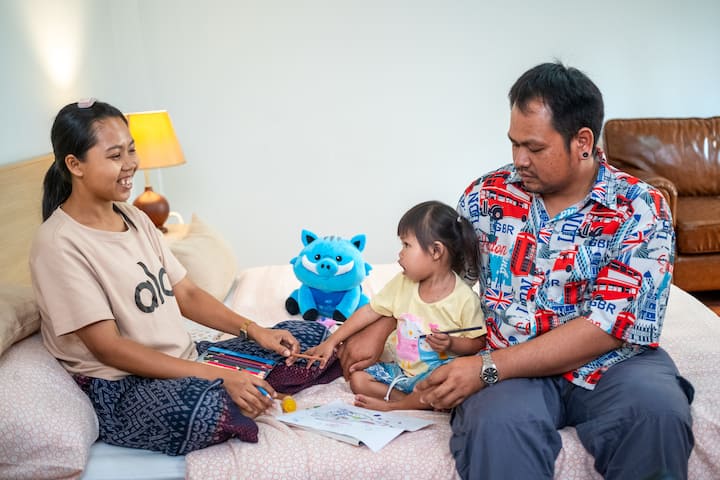 Parents and young daughter sit together on a bed in Maya Suite, sharing a quiet family moment