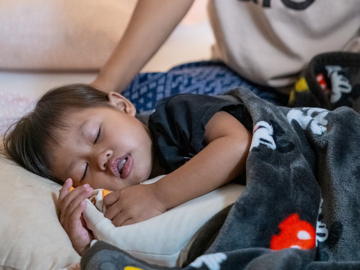 Young child sleeping under a cartoon blanket, resting peacefully in a Thailand host’s cozy home.