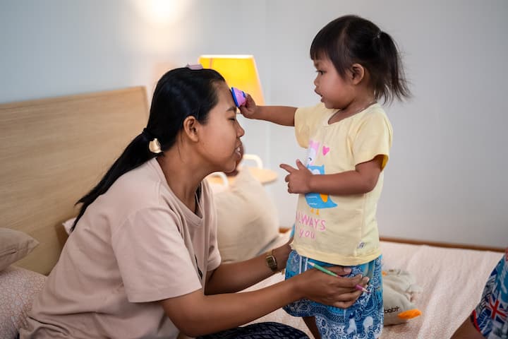 Mother in Thailand interacting with her small child in a cozy, softly lit bedroom
