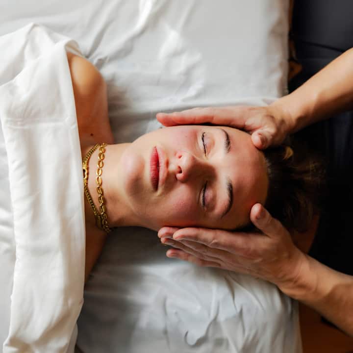 Hands gently performing a massage on a person laying under a white sheet, showcasing a relaxing wellness service experience.