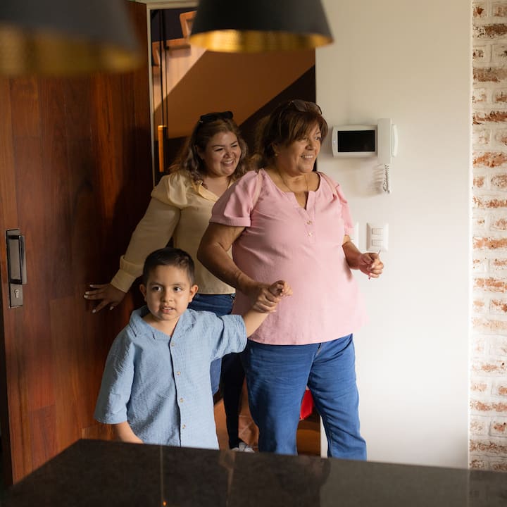 Una madre, su hijo pequeño y la abuela llegan juntos por una entrada bien iluminada al alojamiento que obtuvieron a través de Airbnb.org.