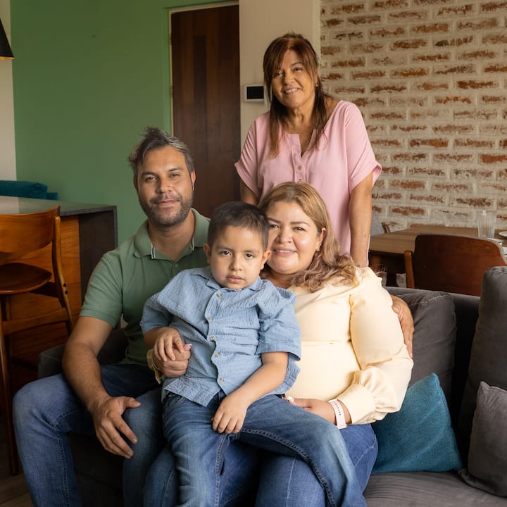 Retrato de un padre, una madre y su hijo pequeño sentados, y una abuela de pie, en el alojamiento que obtuvieron a través de Airbnb.org.