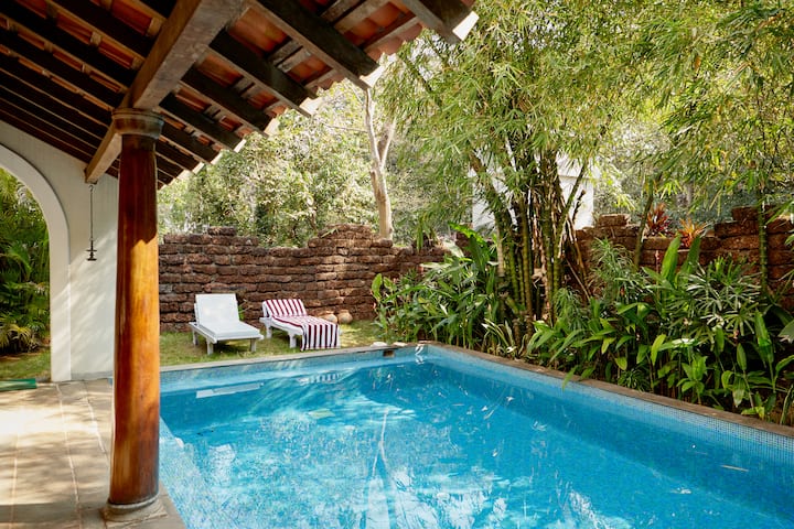 Shaded pool beside lush greenery and stone wall, evoking the tranquil soul of India