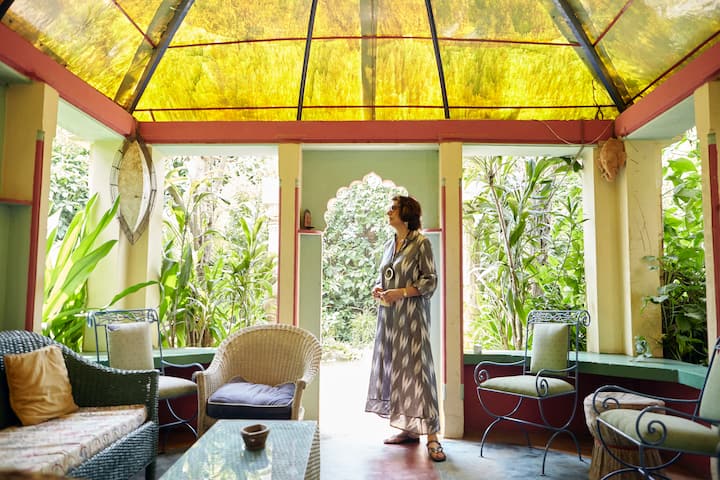 Airbnb host in traditional-inspired dress enjoying a vibrant Indian courtyard lounge surrounded by plants and natural light.