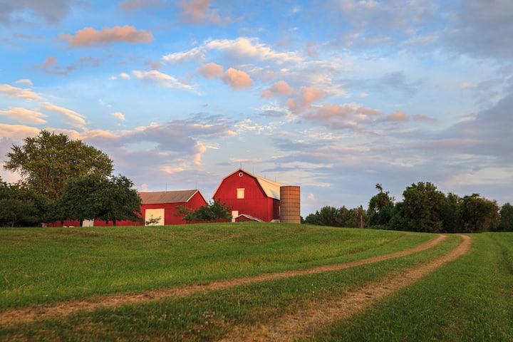 Hudson Valley cider farm with red barns and silo amid green orchards at sunset