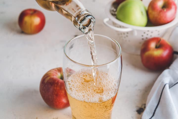 Sparkling apple cider poured into a glass beside fresh apples for the Airbnb x New York Cider Association partnership