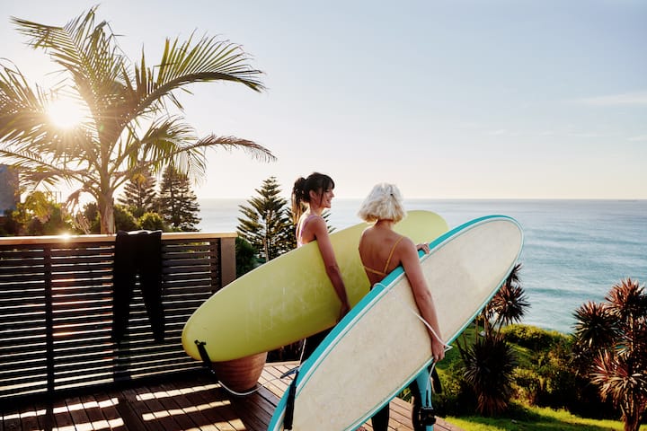 Two people carry surfboards from a deck toward the ocean, highlighting safe, sustained seaside stays
