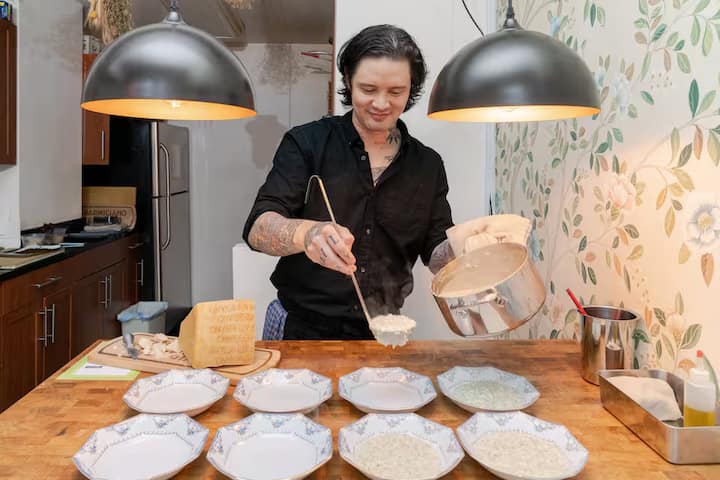 Host in New York City ladling Parmigiano Reggiano risotto into plates on a wooden kitchen counter