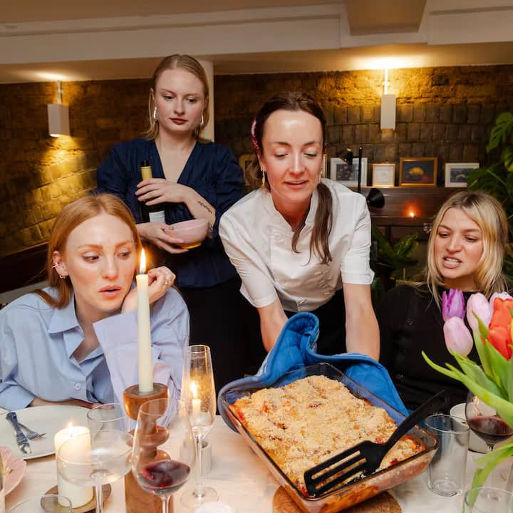 Host in London serving Parmigiano Reggiano baked dish to guests around a candlelit dining table