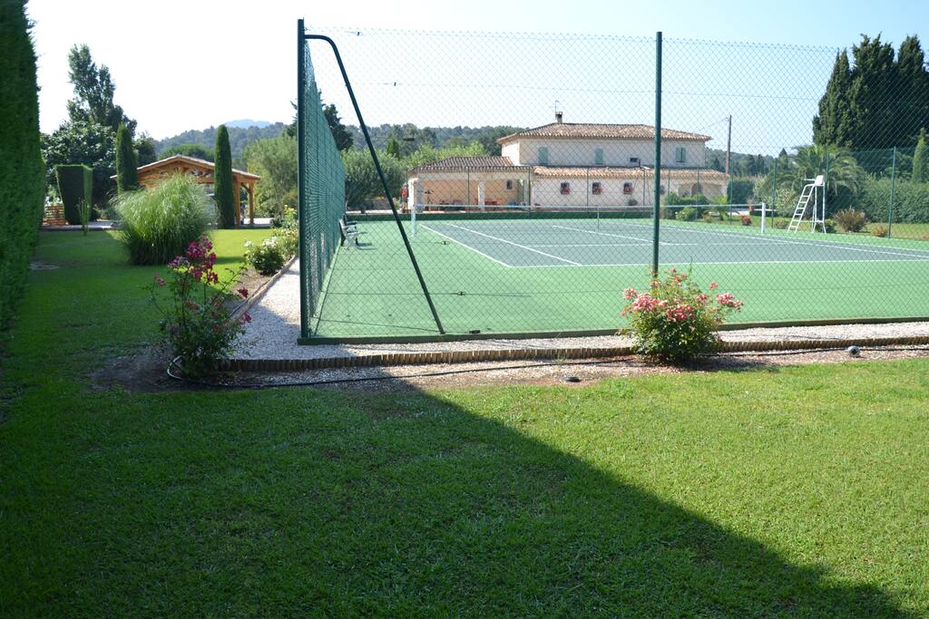 La photo, prise au bout du jardin de derrière, montre le terrain de tennis et l'arrière de la maison.