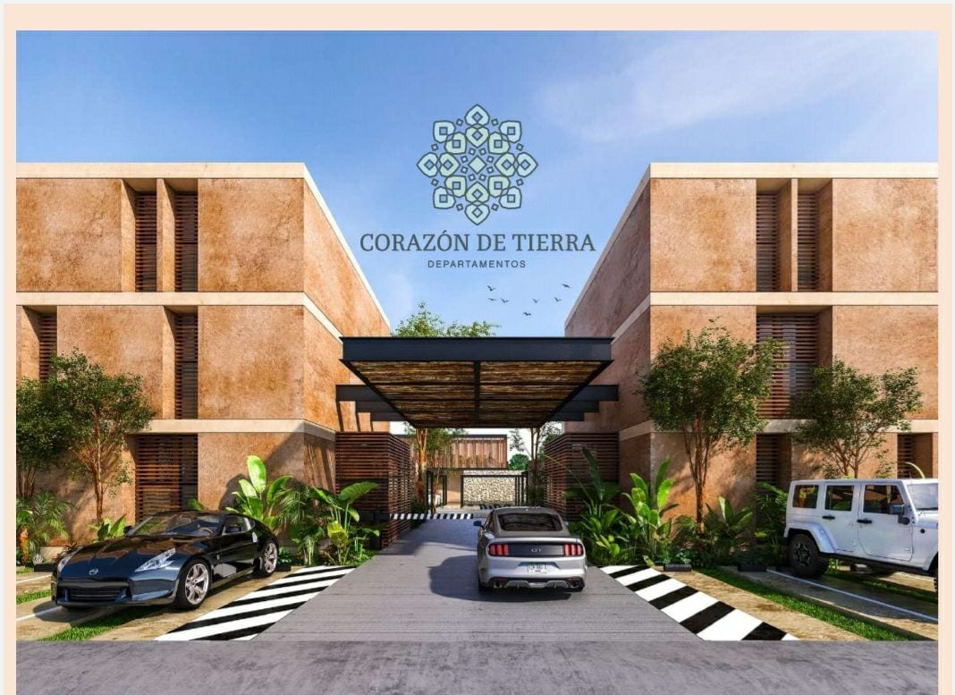 The entrance to Corazón de Tierra features a modern architectural design with a gated entrance. Cars are parked on a driveway lined with greenery, while the logo is displayed prominently above. Clear skies and well-maintained landscaping enhance the welcoming appearance.