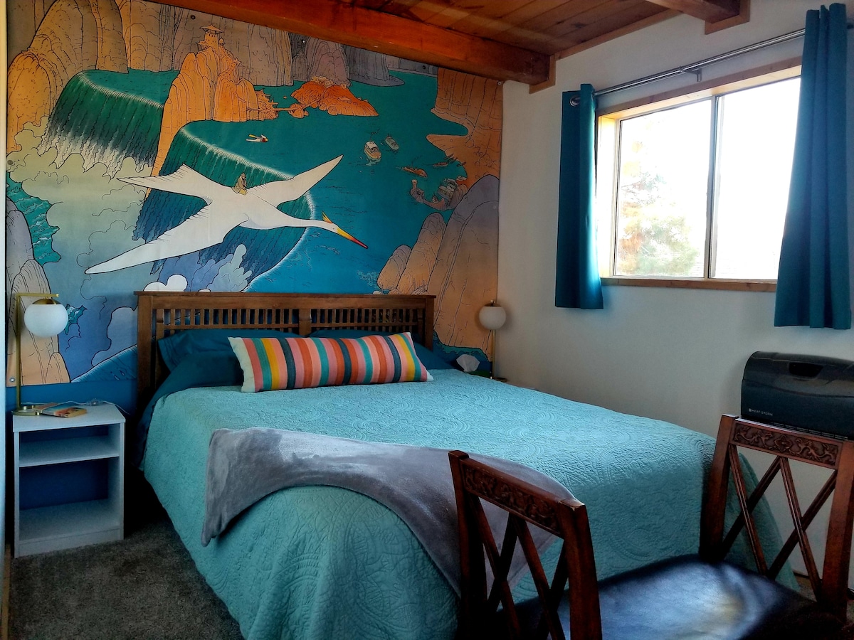 Downstairs bedroom with quilted queen bed. Mural is hand painted on canvas by your host! Original art was by Jean Girard / moebius, the book Edena on the side table for your dreamy reading pleasure. 