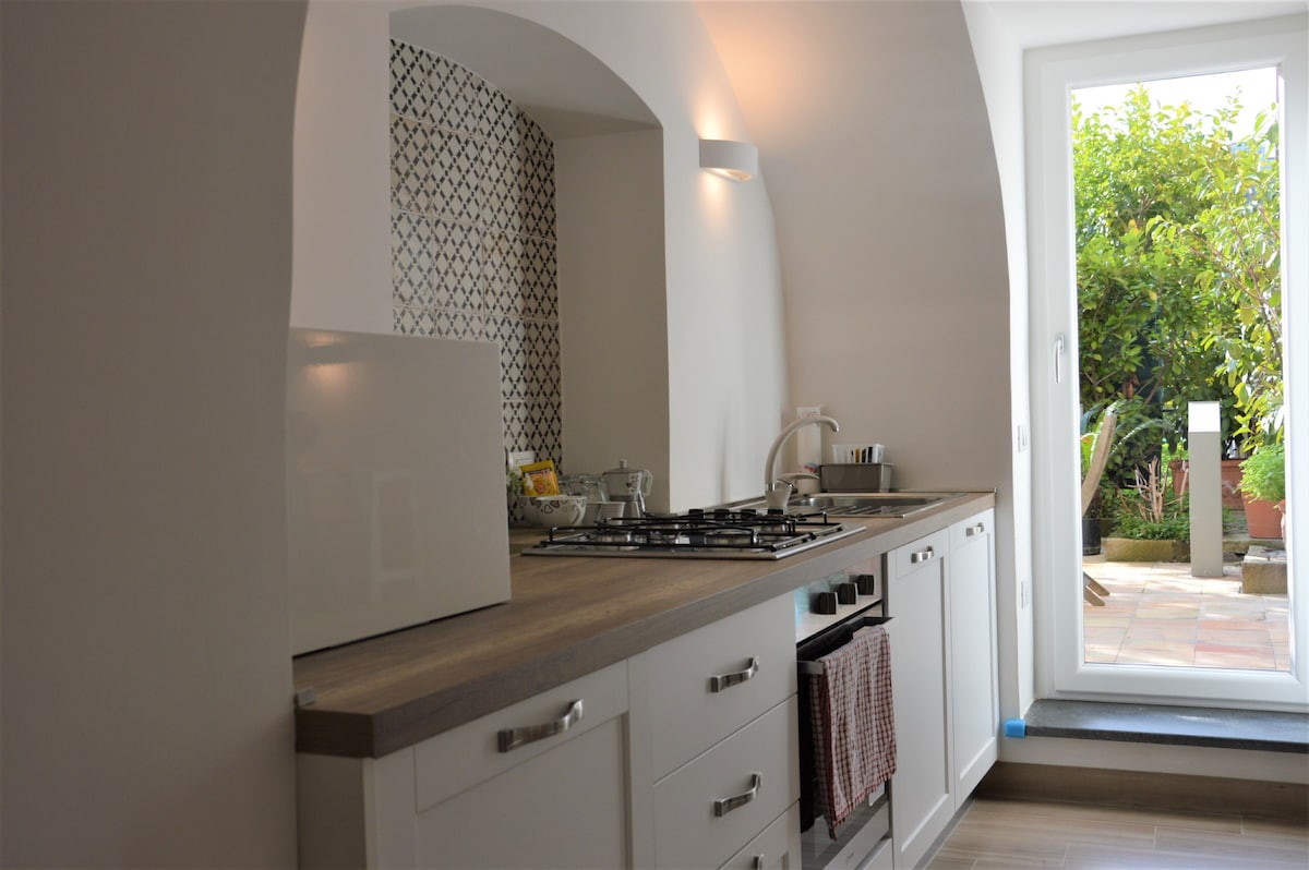 The kitchen features a modern design with fitted cabinetry and a gas stove. Natural light enters through the glass door, which leads to the private garden. Decorative tile work enhances the wall behind the countertop, creating an inviting cooking space.