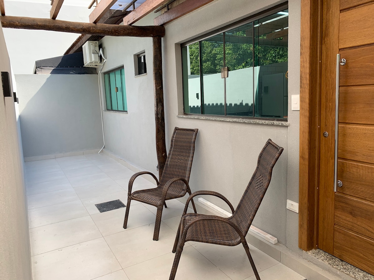 A private patio area is seen, featuring two comfortable chairs positioned under a wooden trellis. A large window allows natural light to brighten the space, with a smooth tiled floor enhancing the open ambiance.